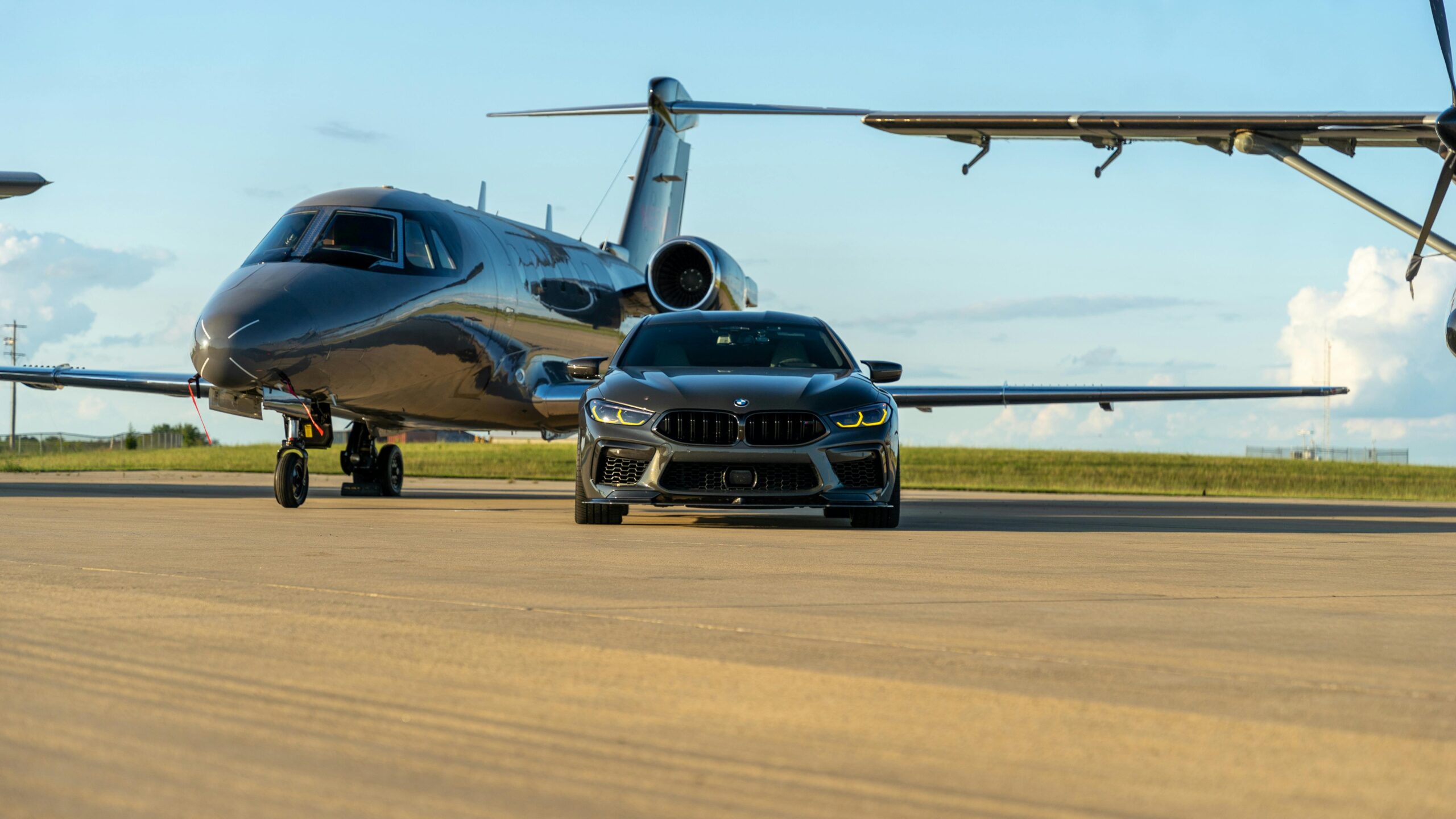 A sleek luxury car parked in front of a private jet on a runway, capturing opulence.
